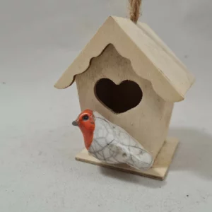 Mini rouge-gorge en céramique Raku devant une petite maison en bois réalisée à la main