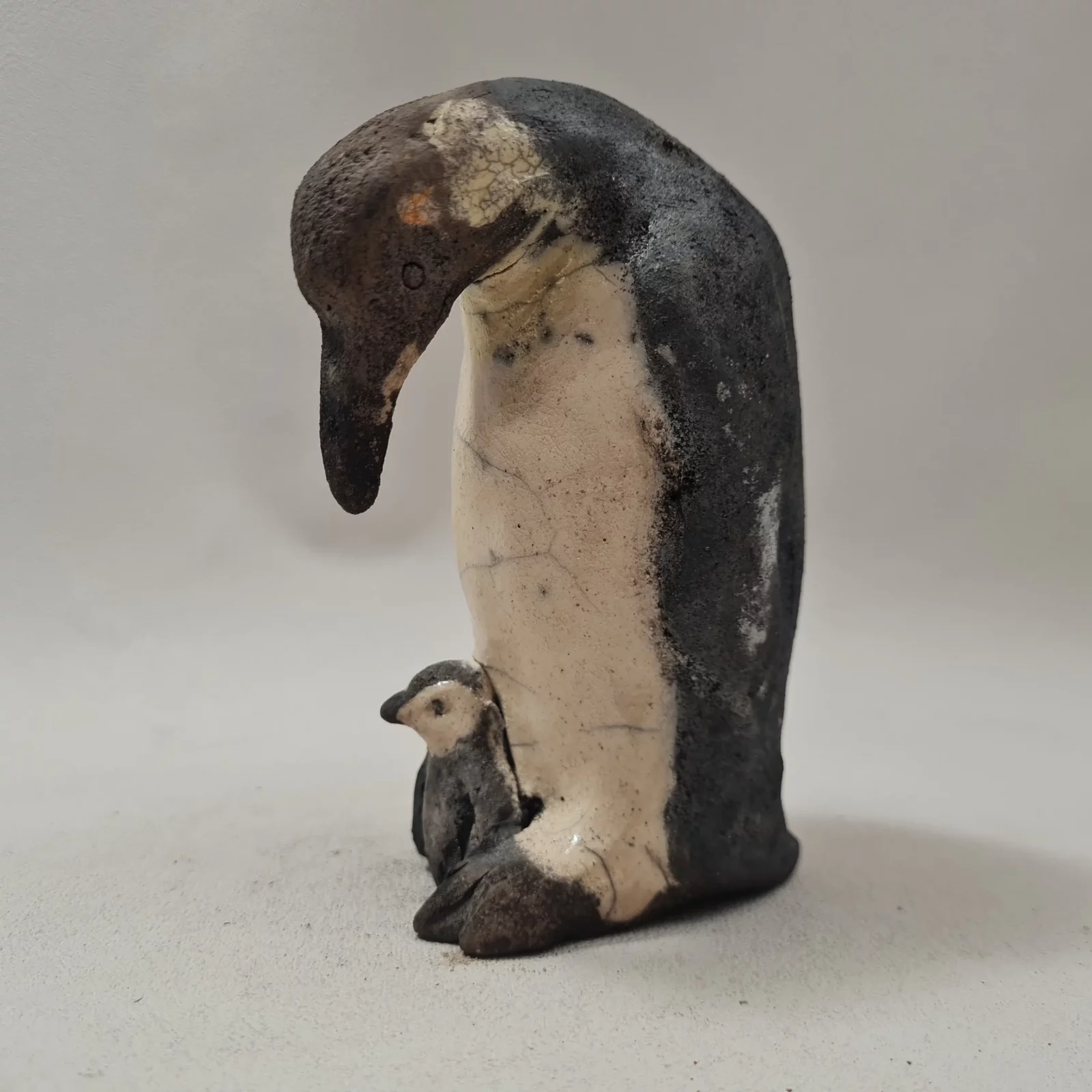 Manchot empereur protégeant son petit sous ses pattes en céramique raku